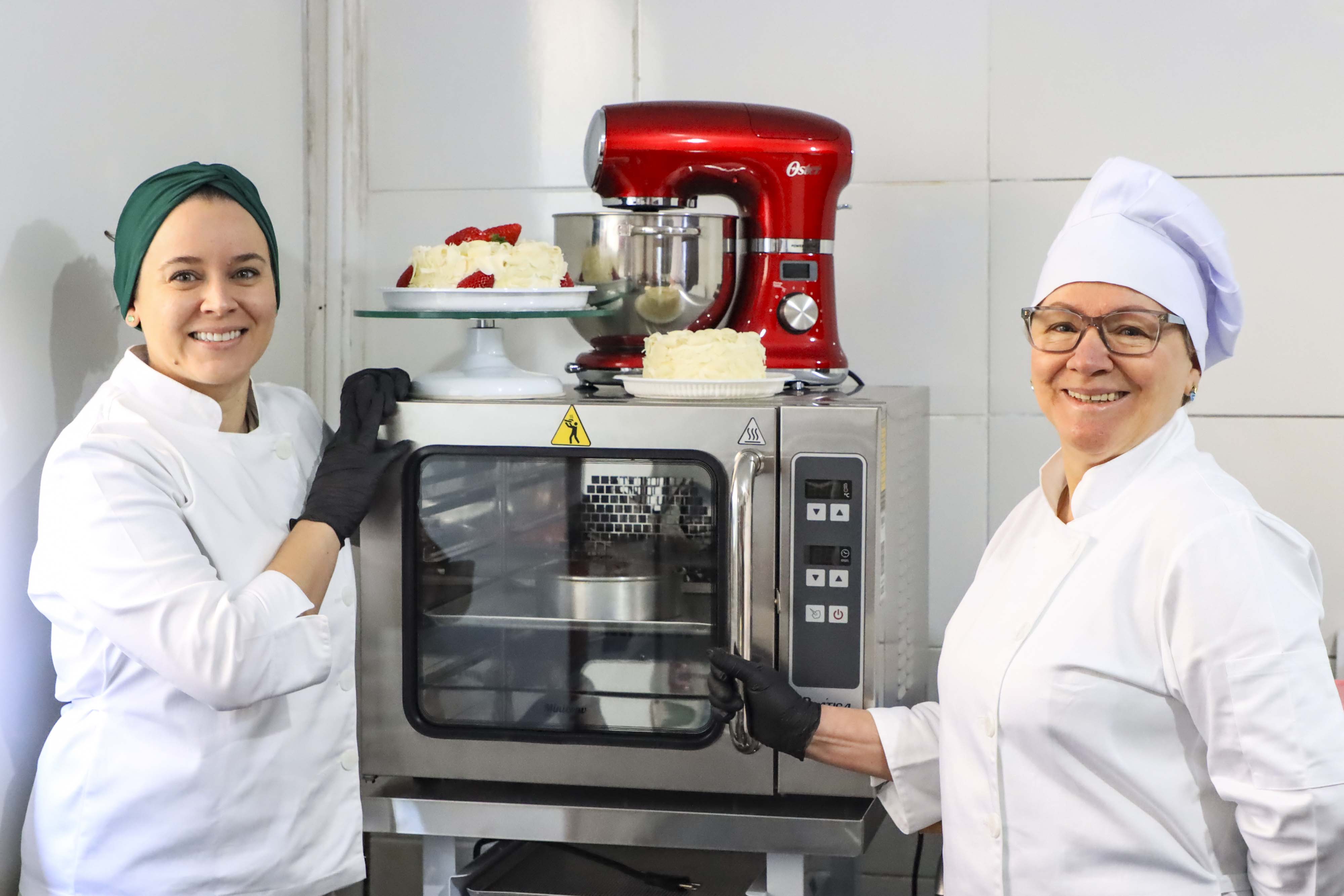 Neusa (à direita), como novo forno e batedeira da empresa familiar adquiridos com financiamento da Fomento Paraná por intermédio da Prefeitura de Curitiba.